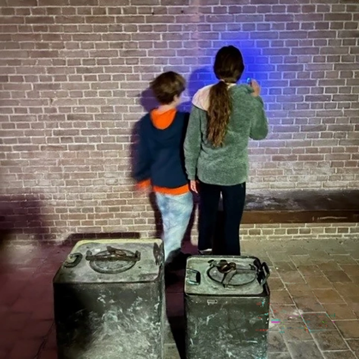 blacklight speurtocht inf fort pampus met twee kinderen die met blauw licht op de muur schijnen, zoekend naar verborgen letters